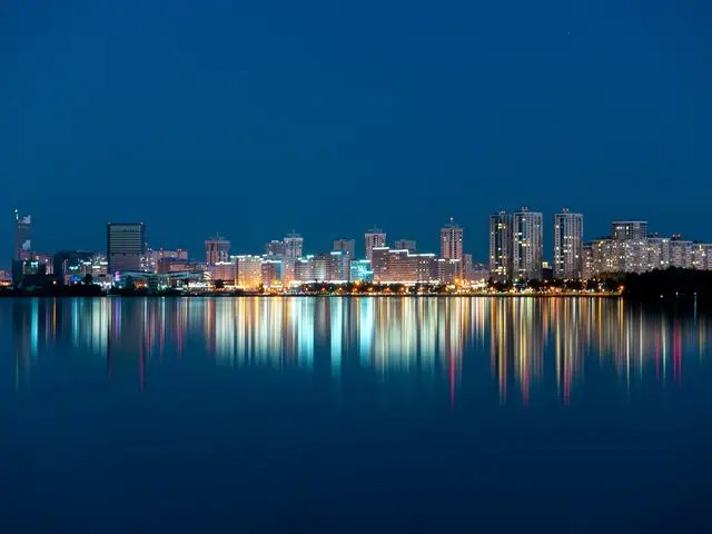 Lit apartment towers along the water at blue hour, their lights reflected in long coloured streaks