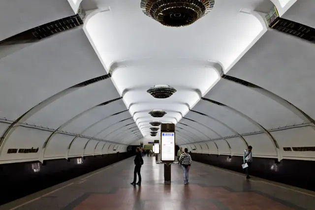 The long white vaulted platform hall of Park Čaliuskincaŭ station, with tiered glass chandeliers down the centre