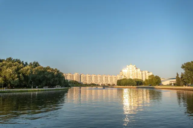 A wide view along the Svislach in golden light, green parkland on the left and a row of modern towers reflected in the water