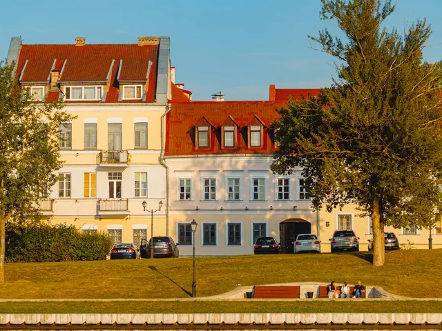 Pastel yellow and white houses with red tiled roofs in Trinity Suburb, lit by low sun above a grassy bank of the Svislach